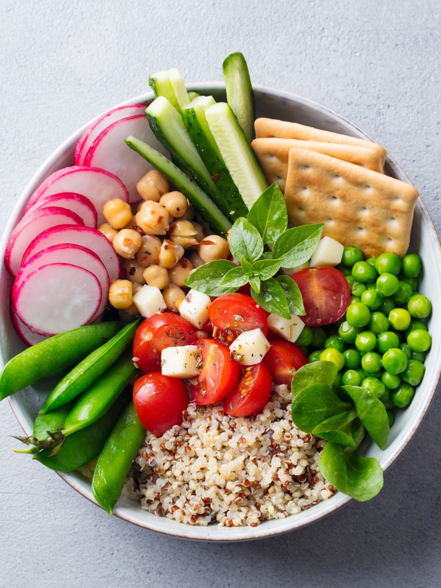 Healthy vegetarian salad. Buddha bowl. Quinoa, chickpea, tomatoes, pea radish cucumber crackers. Grey stone background. Top view